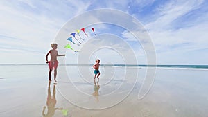 Boys brothers run together holding colorful kites set at beach