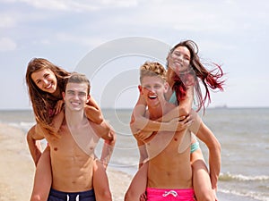 Boys, carrying a their girls on back, at the beach, outdoors. Close-up image of cheerful happy couples.