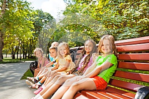 Boys and girls sitting on summer bench in park