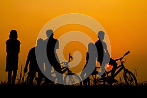 Boys and girls standing and sitting behind a bike with sunset Silhouette concept