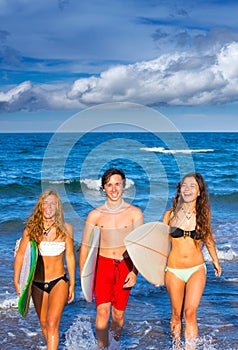 Boys and girls teen surfers coming out from the beach