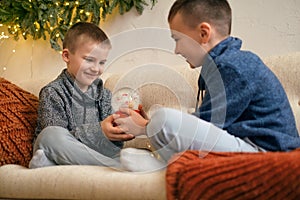 The boys are holding a Christmas snow globe with Santa Claus and flying snowflakes inside.