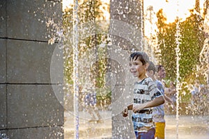 Boys jumping in water fountains. Children playing with a city fountain on hot summer day. Happy friends having fun in fountain.