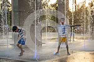 Boys jumping in water fountains. Children playing with a city fountain on hot summer day. Happy friends having fun in fountain.