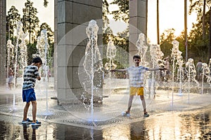Boys jumping in water fountains. Children playing with a city fountain on hot summer day. Happy friends having fun in fountain.