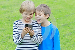 Boys with mobile phone. Children smiling, looking to screen, playing games or using application. Outdoor. Technology