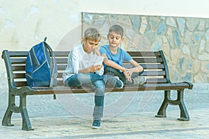 Boys with mobile phone sitting on the bench outdoors