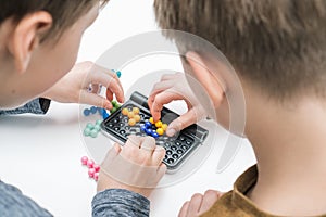 Boys play table tetris on table, from nape view. Hands of players collect colored details on playing board. Board games.