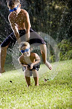 Boys playing leapfrog over lawn sprinkler