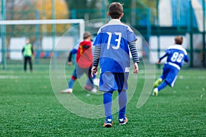 Boys in red and blue sportswear plays  football on field, dribbles ball. Young soccer players with ball on green grass.