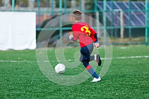 Boys in red and blue sportswear plays  football on field, dribbles ball. Young soccer players with ball on green grass.