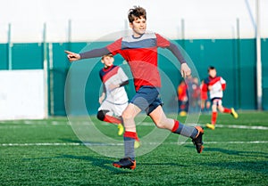 Boys in red and blue sportswear plays football on field, dribbles ball. Young soccer players with ball on green grass. photo