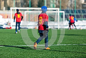 Boys in red sportswear running on a soccer field with snow in the background. Young footballers dribble and kick football ball