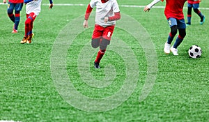 Boys in red and white sportswear plays soccer on green grass field. Youth football game. Children sport competition,