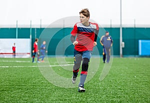 Boys in red white sportswear running on soccer field. Young footballers dribble and kick football ball in game. Training