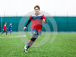 Boys in red white sportswear running on soccer field. Young footballers dribble and kick football ball in game. Training