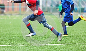 Boys in red white sportswear running on soccer field. Young footballers dribble and kick football ball in game. Training