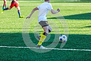 Boys in red white sportswear running on soccer field. Young footballers dribble and kick football ball in game. Training