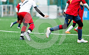 Boys in red white sportswear running on soccer field. Young footballers dribble and kick football ball in game. Training