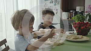 The boys rolling up pancakes with strawberries in tube. Boys eating pancakes.