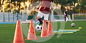 Boys running soccer balls between training cones. European football sports summer camp for youth athletes