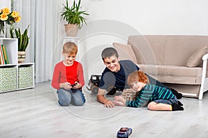 The boys sit on the floor in the room and play with the machine with the remote control