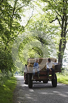 Boys Sitting On Back Of Trailer On Country Lane