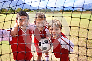 Boys, soccer player and ball on goal net, smile and happy for game, field and child. Outdoor, playful and sport for