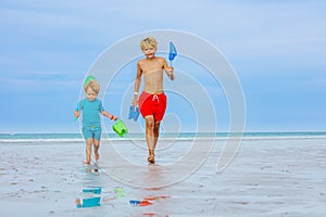 Boys walk on a beach hold buckets and hoop-net catching crabs