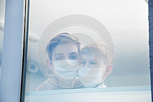 Boys wearing protective masks cuddling and loking through the window of hospital