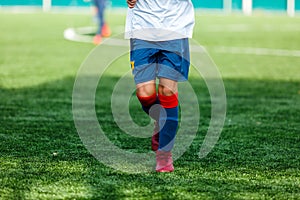 Boys in white and blue sportswear plays football on field, dribbles ball. Young soccer players with ball on green grass.