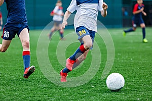 Boys in white and blue sportswear plays football on field, dribbles ball. Young soccer players with ball on green grass. Training photo