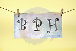 BPH Benign Prostatic Hyperplasia lettering on colored paper hanging in front of a yellow background with a rope and clothespins