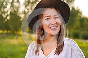 Braces on the teeth, a girl of Asian appearance in a white T-shirt and a dark hat, looking at the camera and smiling