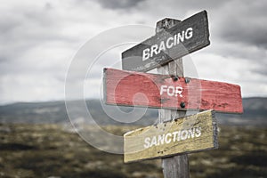 bracing for sanctions text quote on german flag painted on wooden signpost outdoors in nature.