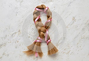 Braided red hair for donation with pink ribbon on grunge background