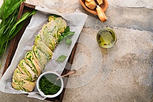 Braided wild garlic pesto brioche. Homemade raw or uncooked fresh pull apart bread with wild garlic pesto on wooden board on old