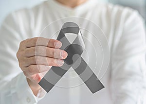 Brain cancer awareness with grey ribbon on person helping hand, symbolic bow color for Brain tumor, Allergies, Alpha-1 Antitrypsin photo
