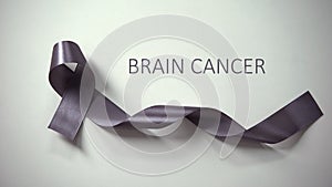 Brain cancer inscription, gray ribbon lying on table, awareness campaign, ad