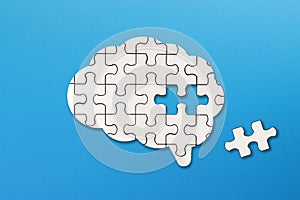 Brain shaped white jigsaw puzzle on blue background, a missing piece of the brain puzzle, mental health and problems with memory