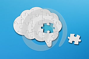 Brain shaped white jigsaw puzzle with copy space on blue background, a missing piece of the brain puzzle, mental health and proble