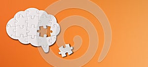 Brain shaped white jigsaw puzzle on orange background, a missing piece of the brain puzzle, mental health and problems with memory