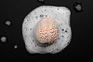 Brainwashing, lower critical thinking and mind control concept with human brain washing in soapy bubbles isolated on black