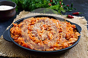 Braised cabbage from tomato sauce in a cast-iron frying pan on a black background. Lenten menu. Diet low-calorie vegetable dish