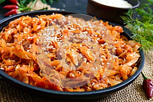 Braised cabbage from tomato sauce in a cast-iron frying pan on a black background. Lenten menu. Diet low-calorie vegetable dish.