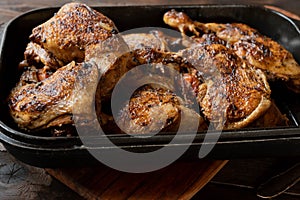 Braised chicken legs in a rosting pan on dark wooden background.