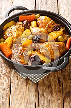 Braised chicken meat with spicy sauce, prunes, carrots, potatoes, olives and onions close-up in a frying pan. Vertical photo