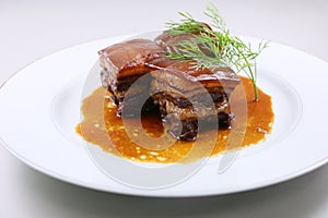 Braised pork meat in Chinese style with herbs on white plate