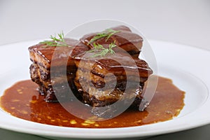 Braised pork meat in Chinese style with herbs on white plate