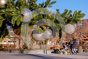 Branch of artificial Christmas tree with white christmas balls on city street outdoors at sunny day